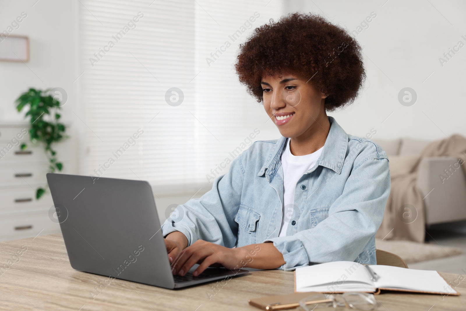 Photo of Young woman using laptop at wooden desk in room