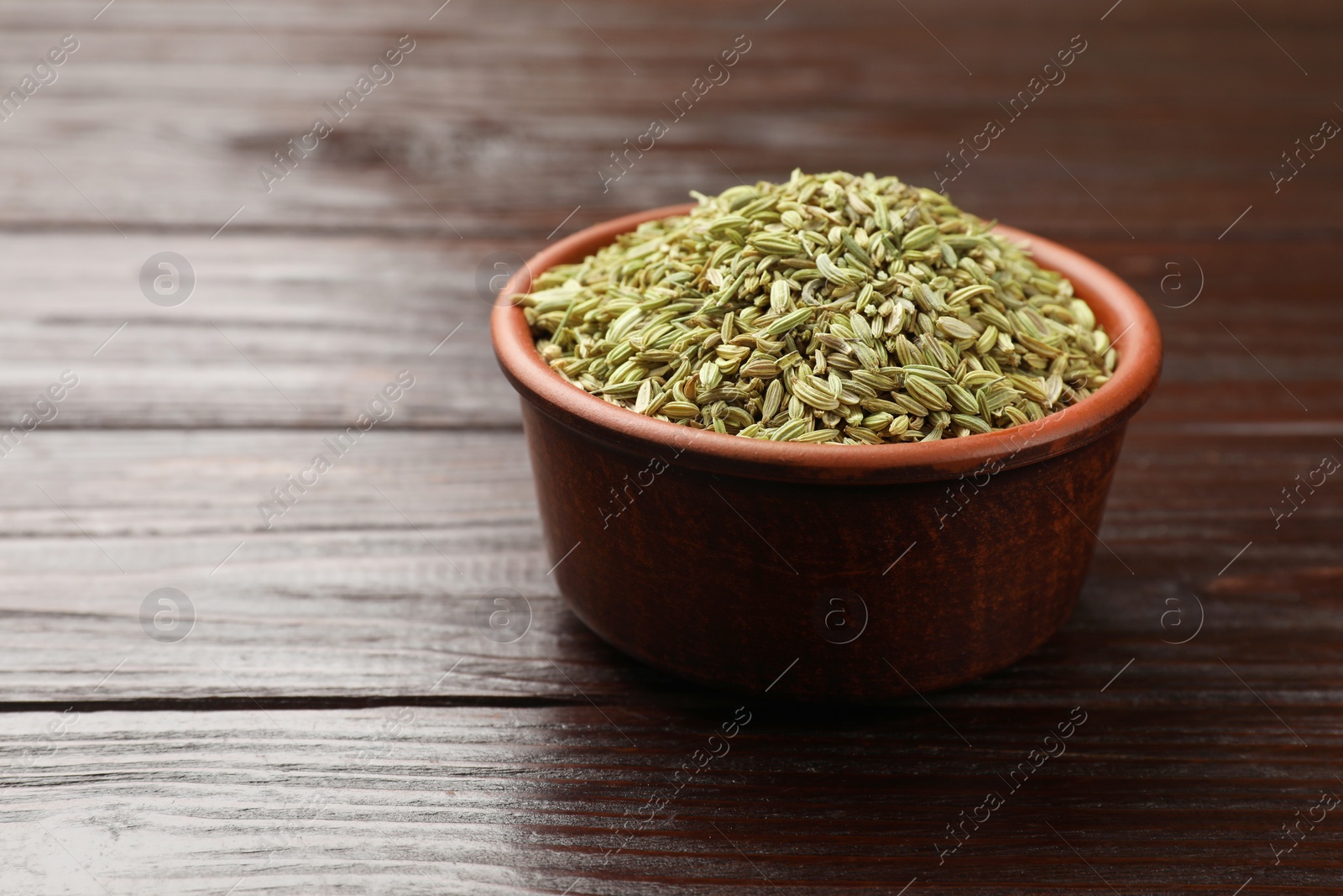 Photo of Fennel seeds in bowl on wooden table, closeup. Space for text