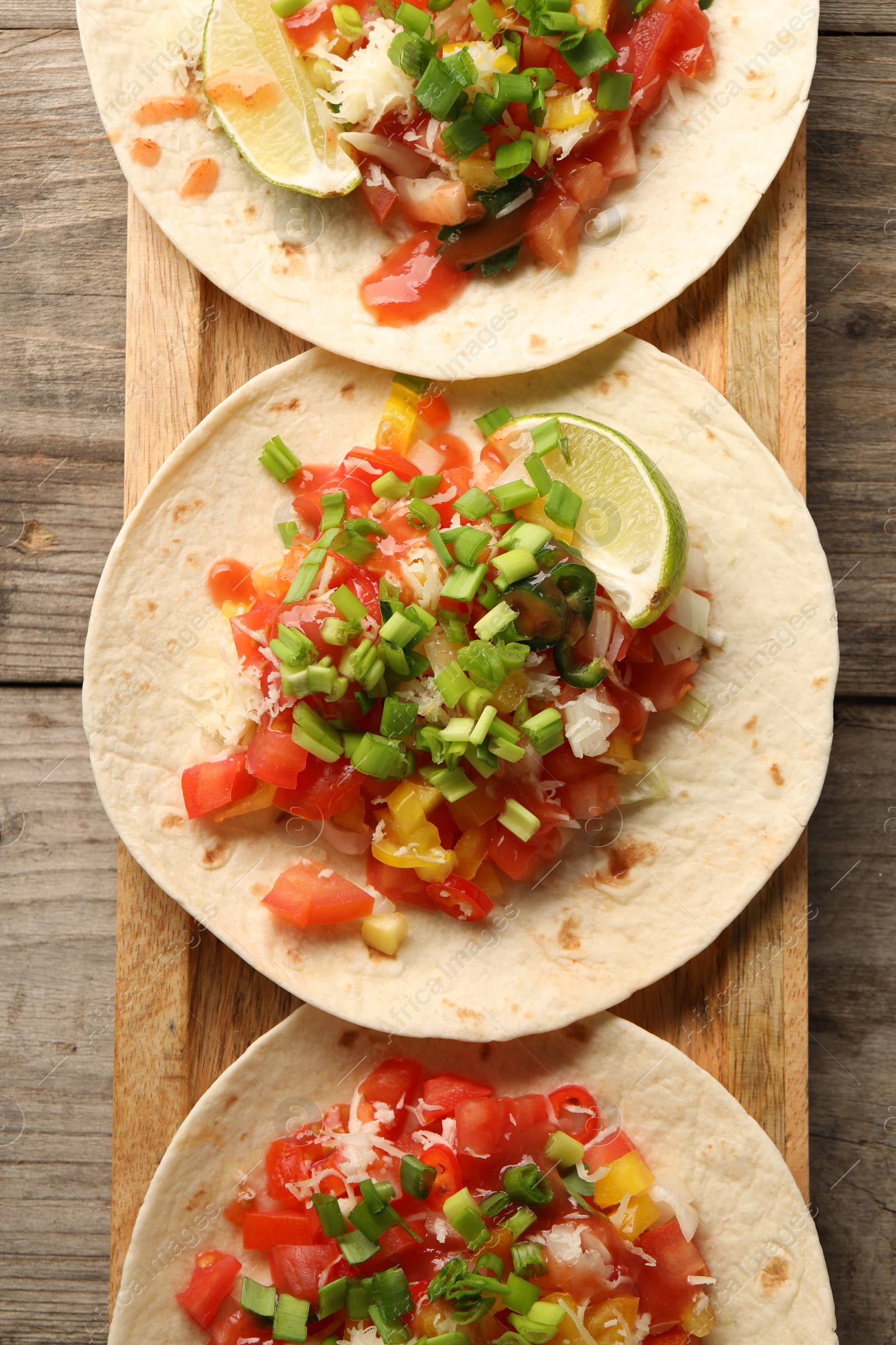 Photo of Delicious tacos with vegetables, green onion, lime and ketchup on wooden table, top view