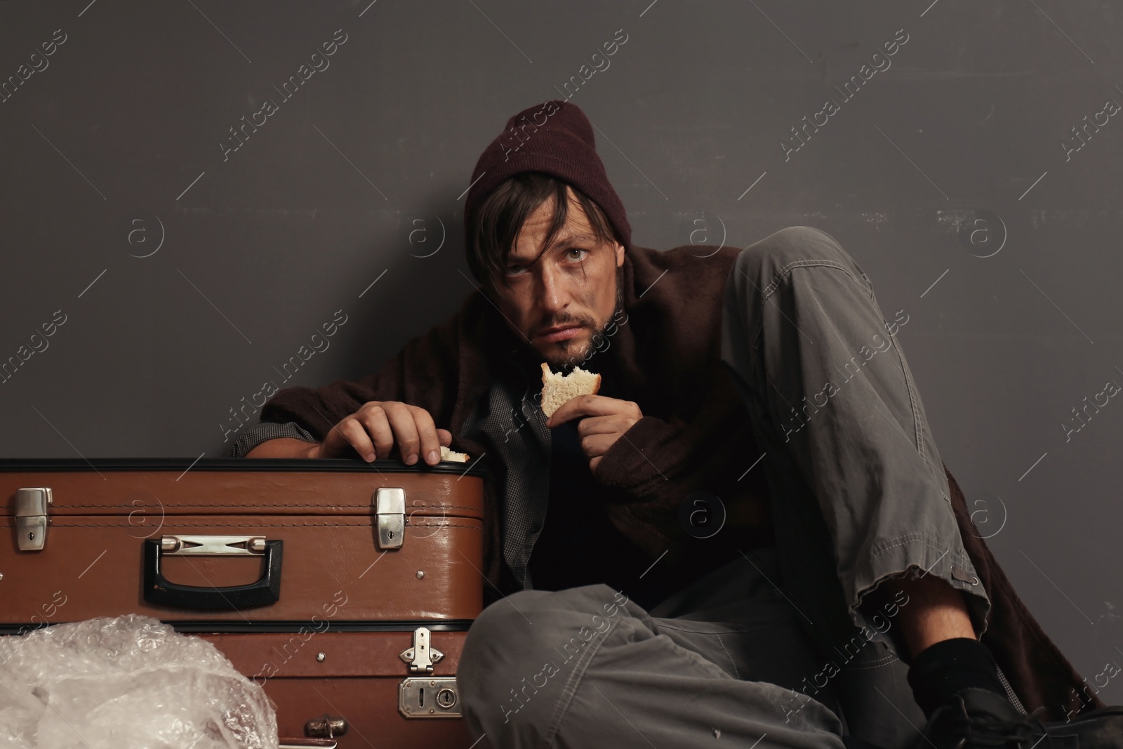 Photo of Poor homeless man eating near dark wall