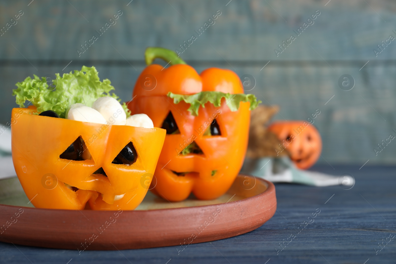 Photo of Bell peppers with black olives and lettuce as Halloween monsters on blue wooden table