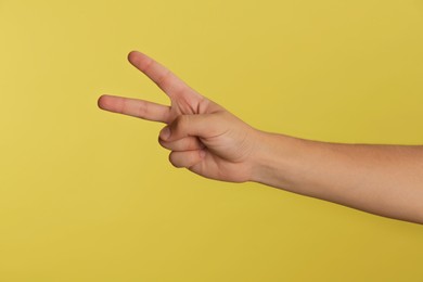 Photo of Teenage boy showing two fingers on yellow background, closeup