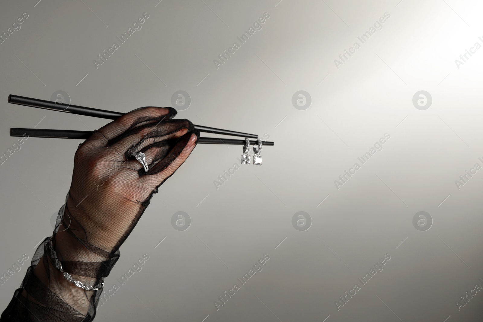 Photo of Woman presenting elegant jewelry on dark beige background, closeup. Space for text