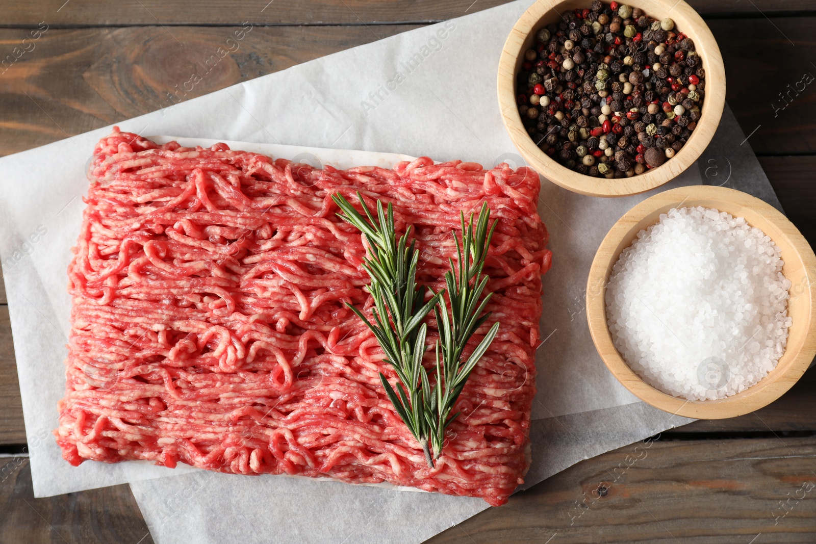 Photo of Raw ground meat, spices and rosemary on wooden table, top view