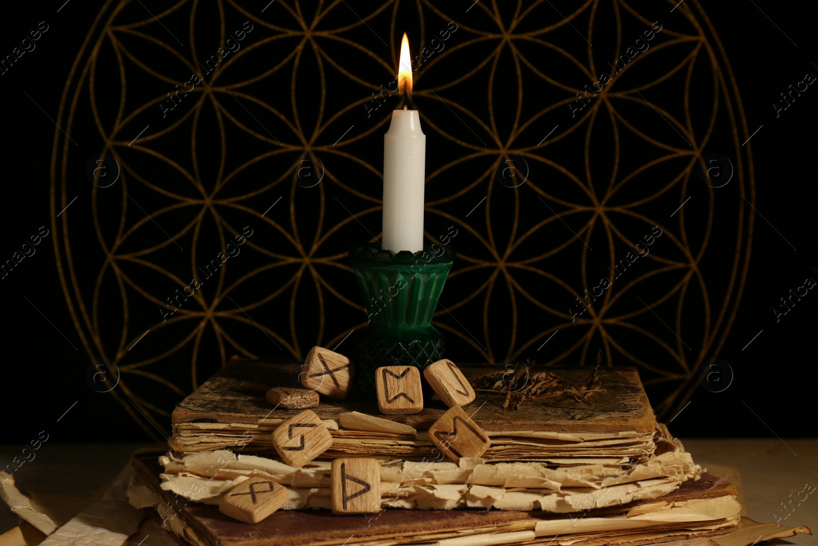 Photo of Wooden runes, old books and burning candle on grey table