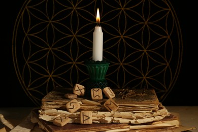 Photo of Wooden runes, old books and burning candle on grey table