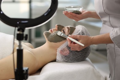 Photo of Cosmetologist applying mask on woman's face in clinic, closeup