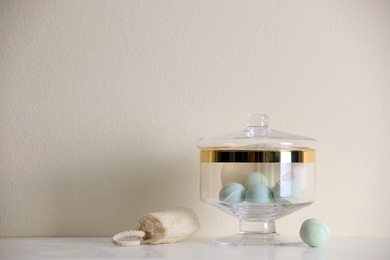 Photo of Jar with bath bombs and bath sponge on table against beige background. Space for text