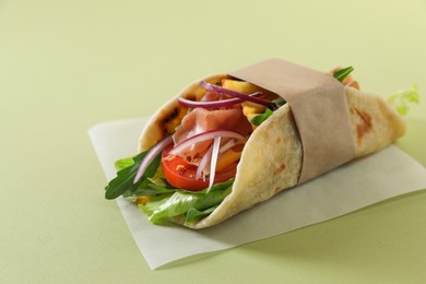 Photo of Delicious pita wrap with jamon, french fries and vegetables on light green background