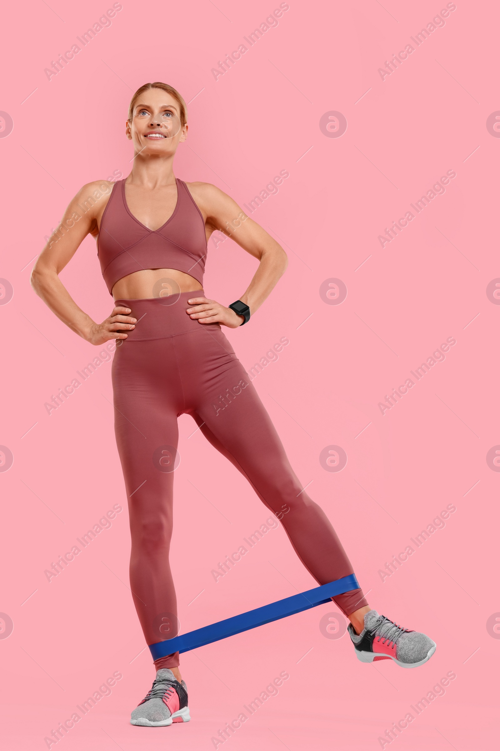 Photo of Woman exercising with elastic resistance band on pink background, low angle view