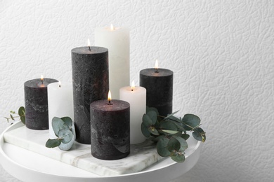 Photo of Set of burning candles and green branches on table at white wall, space for text