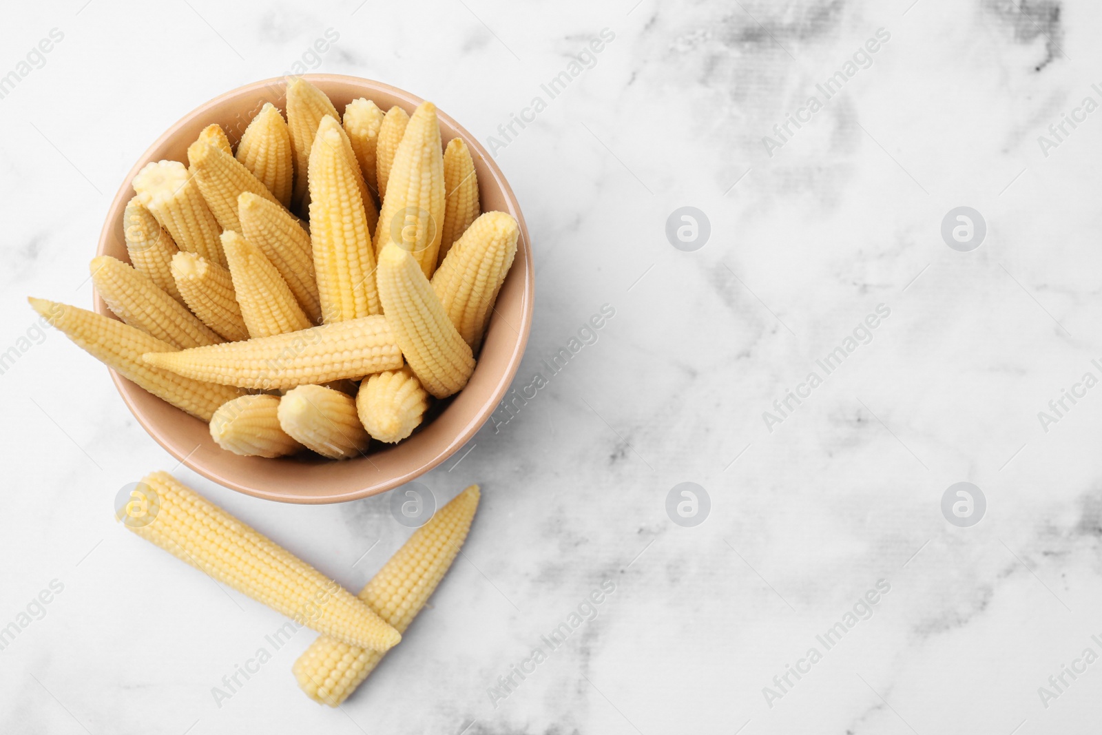 Photo of Bowl and pickled baby corn on white marble table, flat lay. Space for text