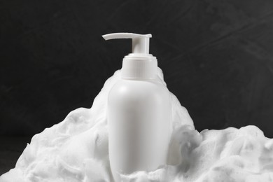 Dispenser with cleansing foam on dark grey background, closeup. Cosmetic product