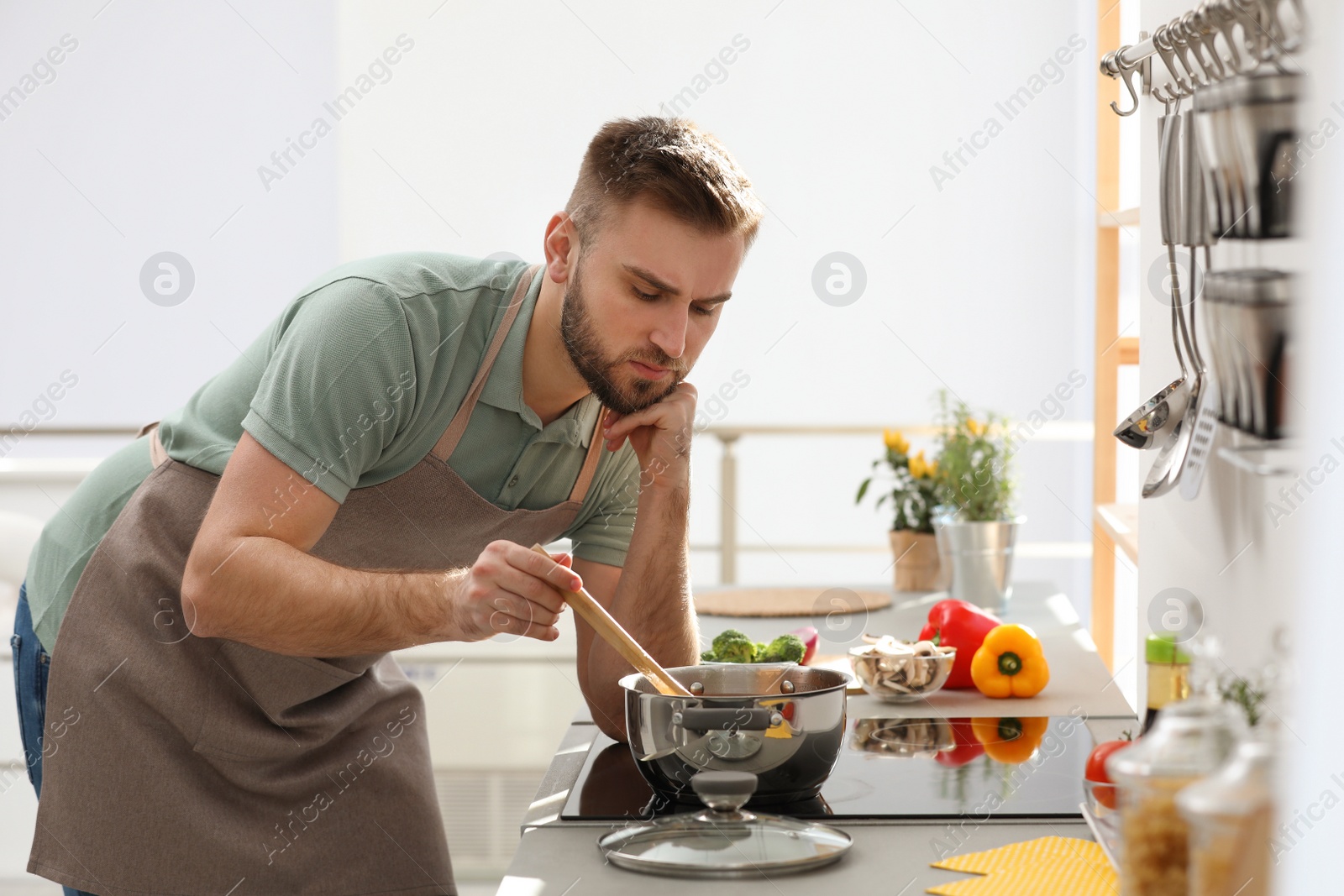 Photo of Young man cooking delicious soup in kitchen