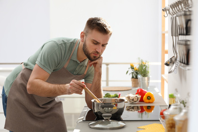 Young man cooking delicious soup in kitchen