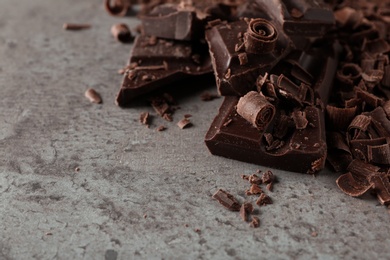 Photo of Curls and pieces of tasty chocolate on gray background, closeup with space for text