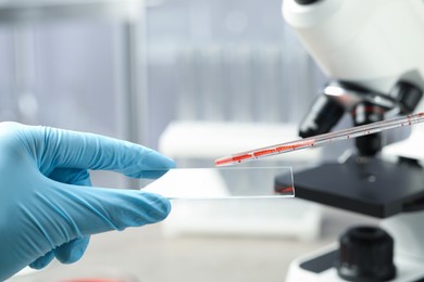 Scientist dripping sample of red liquid onto microscope slide in laboratory, closeup