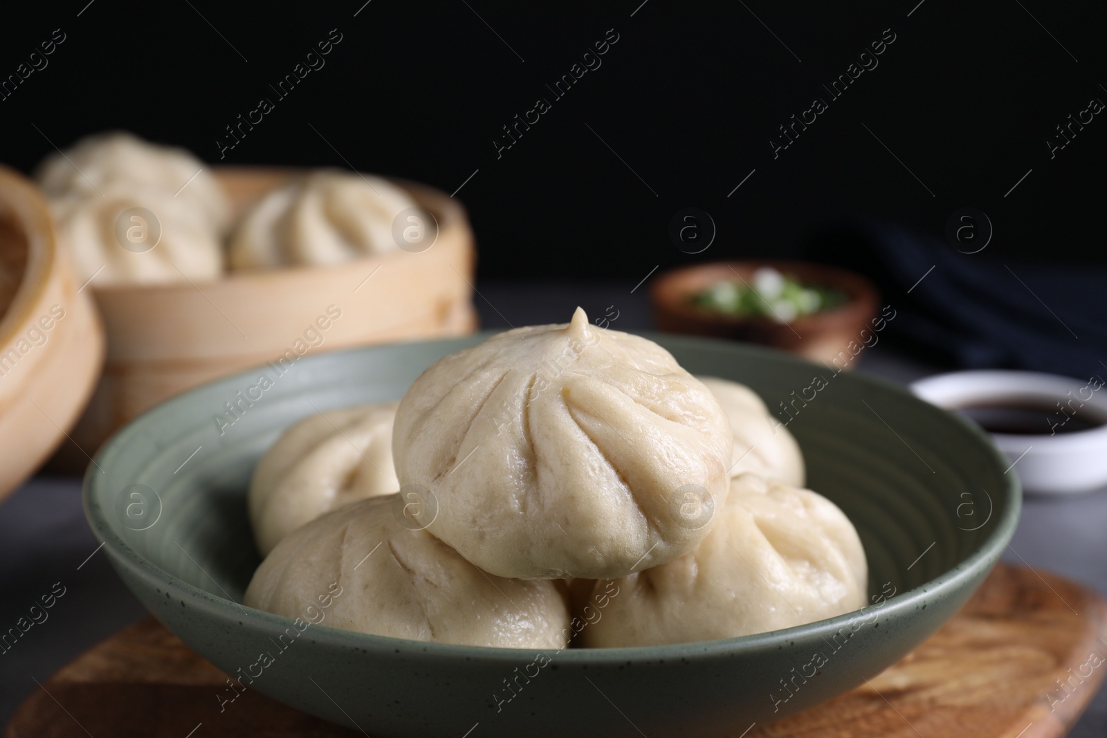 Photo of Delicious bao buns (baozi) in bowl on grey table, closeup