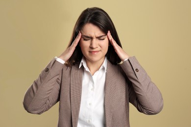 Photo of Young woman suffering from migraine on beige background