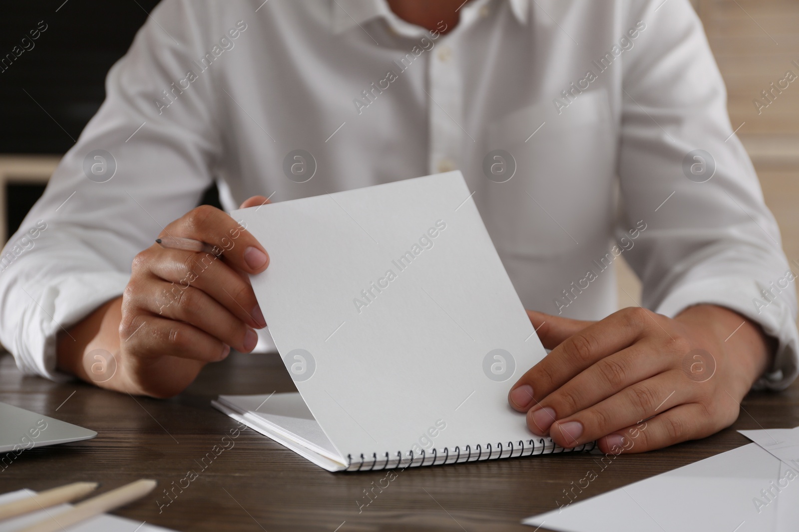 Photo of Man with pencil and notepad at wooden table, closeup