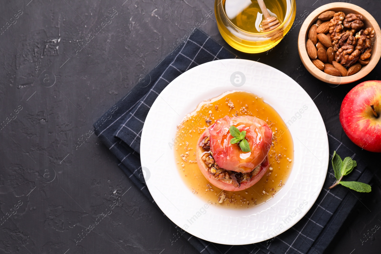 Photo of Tasty baked apple with nuts, honey and mint on gray textured table, flat lay. Space for text