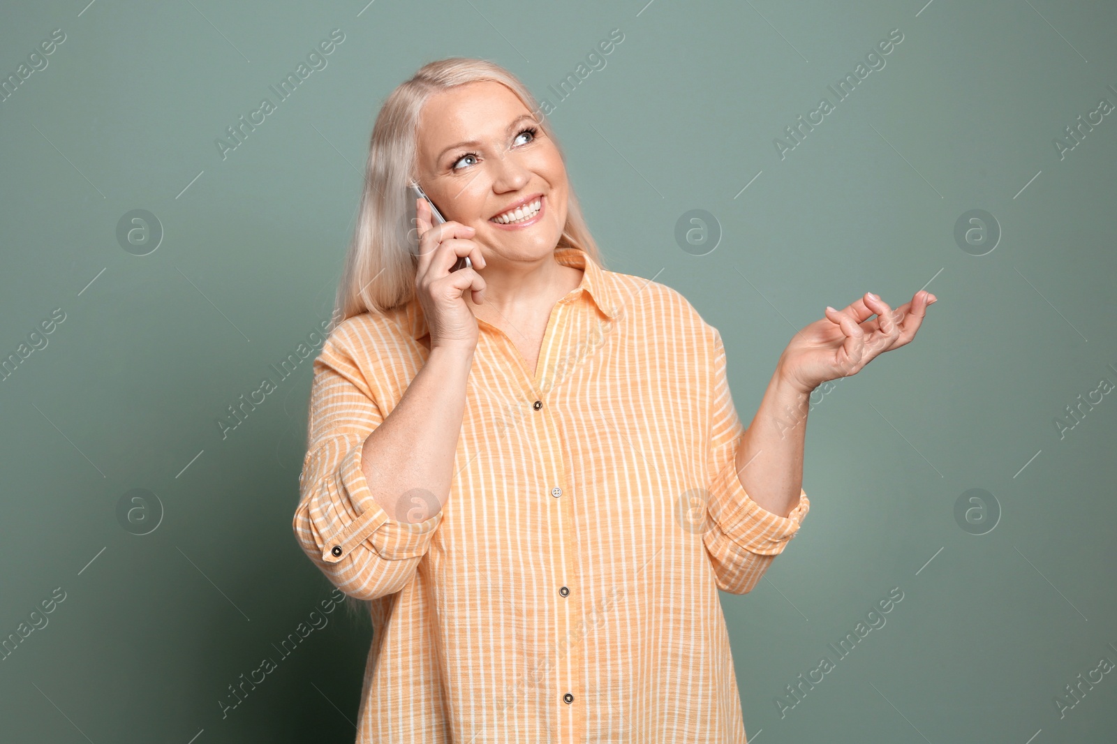 Photo of Mature woman talking on mobile phone against color background