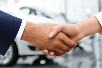 Woman buying car and shaking hands with salesman against blurred auto, closeup