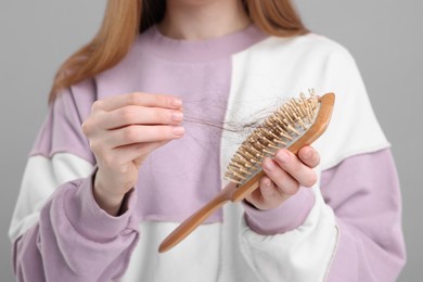 Photo of Woman untangling her lost hair from brush on light grey background, closeup. Alopecia problem