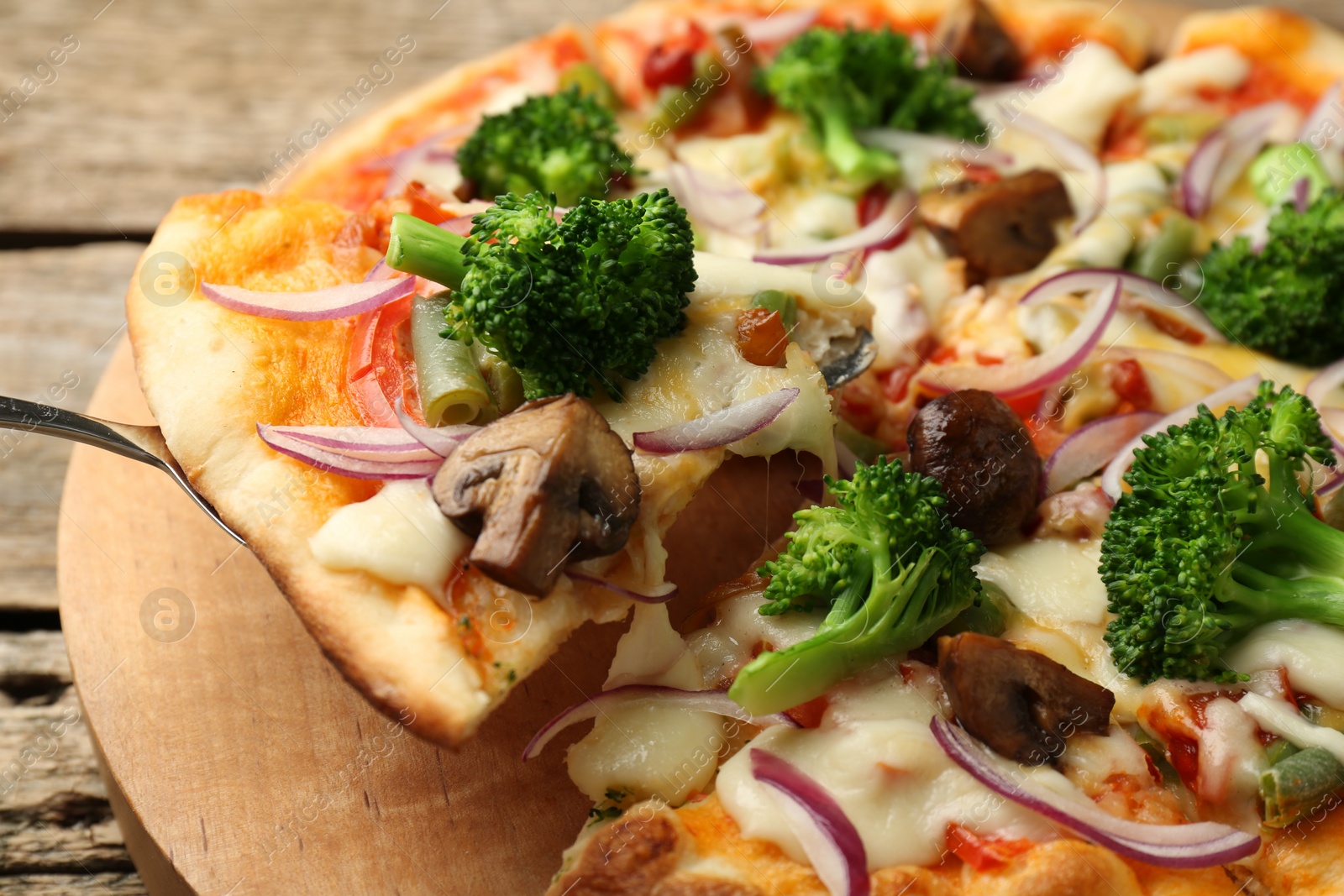 Photo of Taking piece of delicious vegetarian pizza at wooden table, closeup