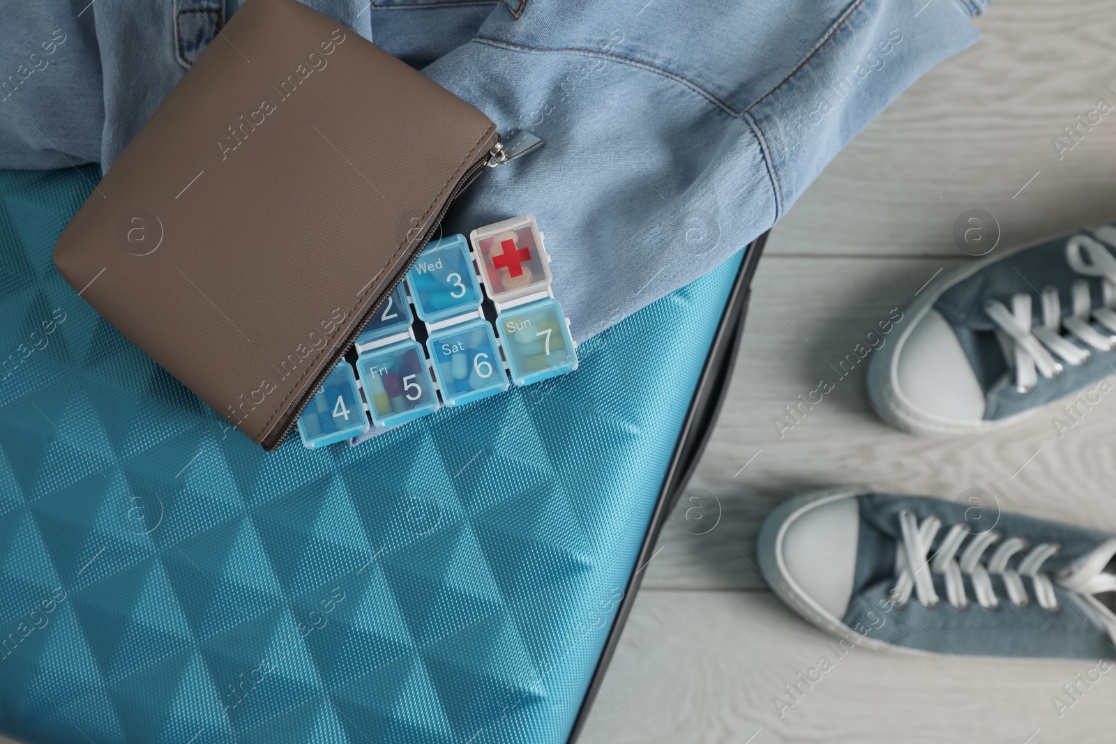 Photo of Suitcase with pill box, denim shirt and shoes on floor, flat lay
