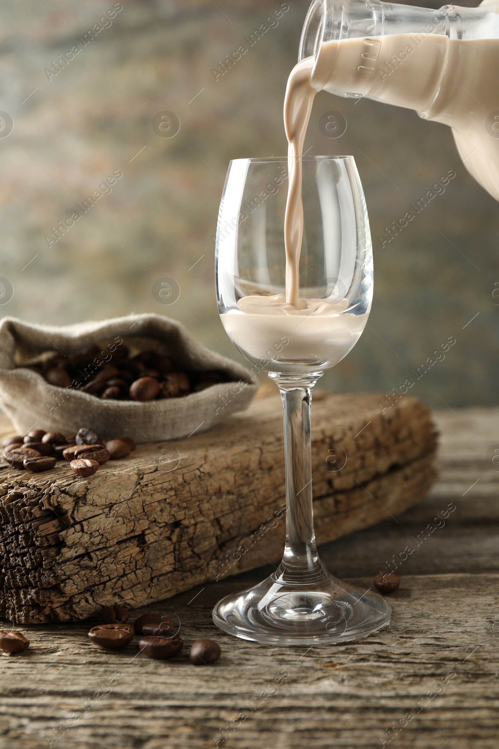 Photo of Pouring coffee cream liqueur into glass at wooden table, closeup