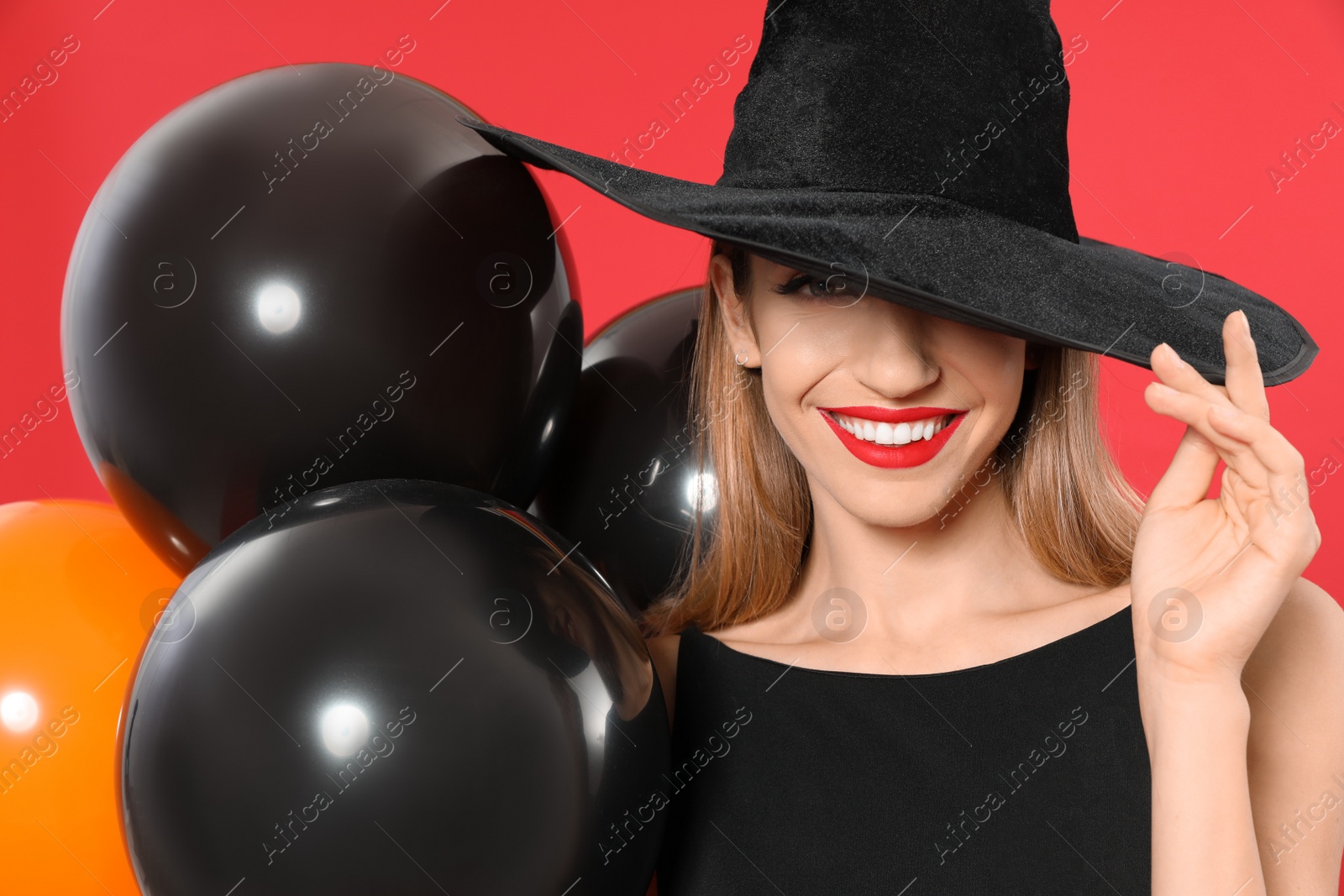 Photo of Beautiful woman wearing witch costume with balloons for Halloween party on red background