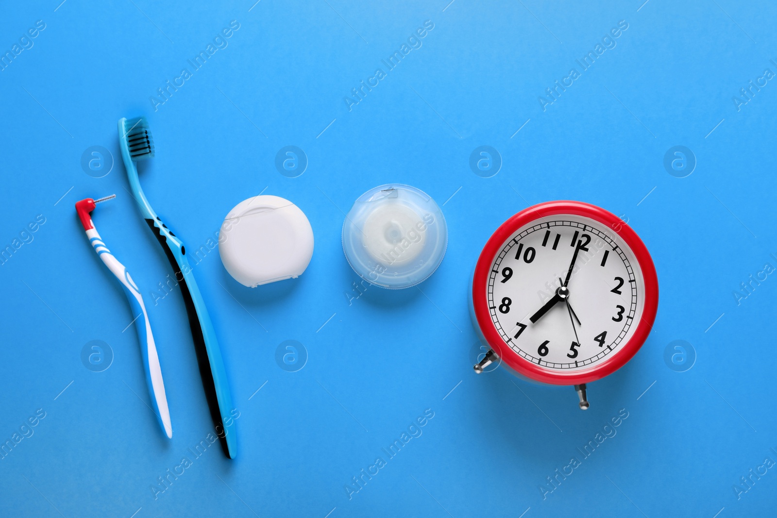 Photo of Containers with dental floss, toothbrushes and alarm clock on light blue background, flat lay