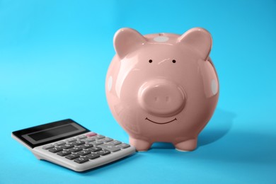 Photo of Calculator and pink piggy bank on light blue background