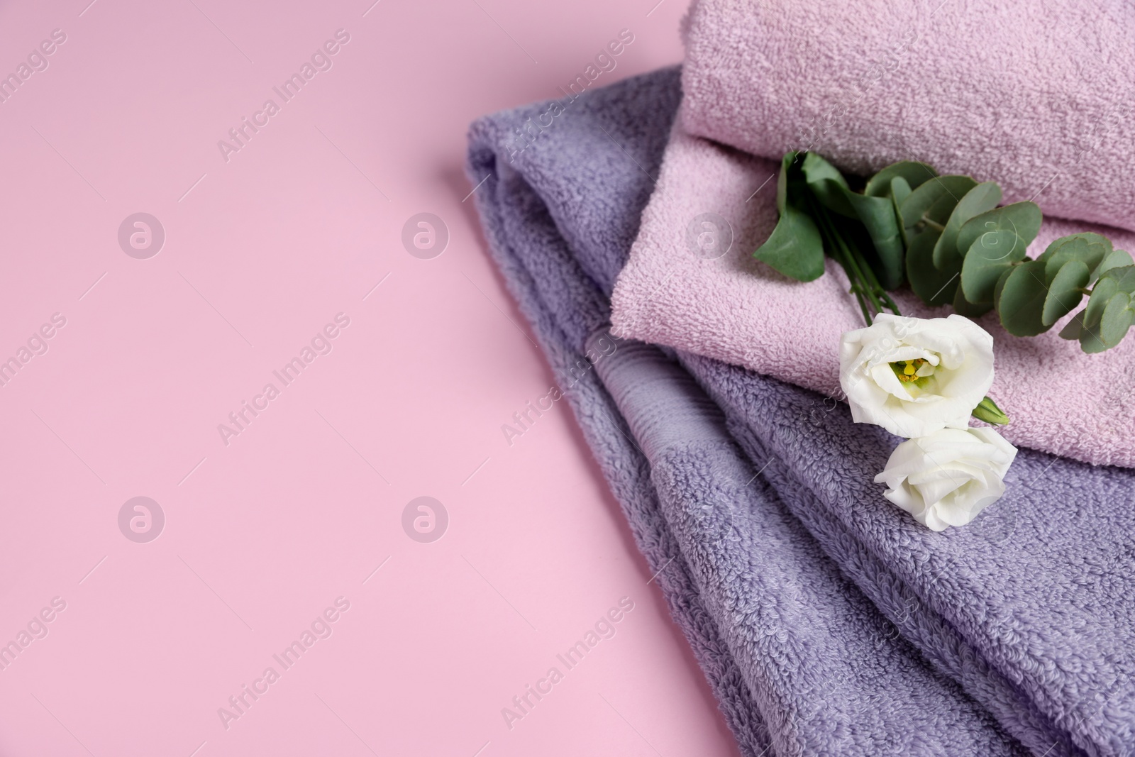 Photo of Soft folded towels with flowers and eucalyptus branch on pink background, closeup. Space for text