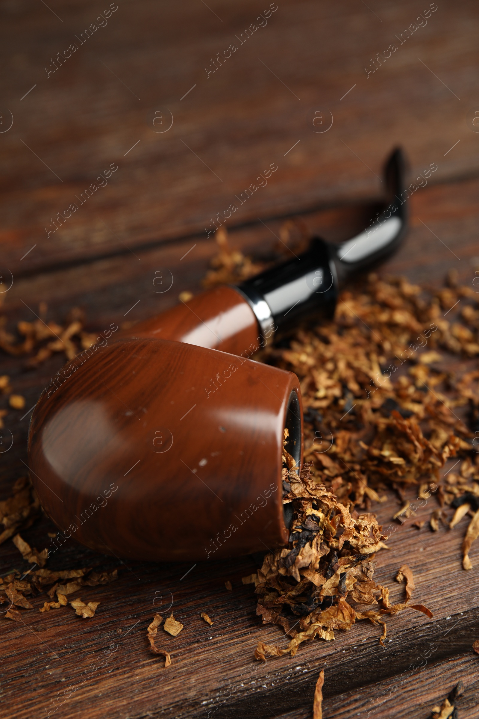 Photo of Smoking pipe and dry tobacco on wooden table, closeup