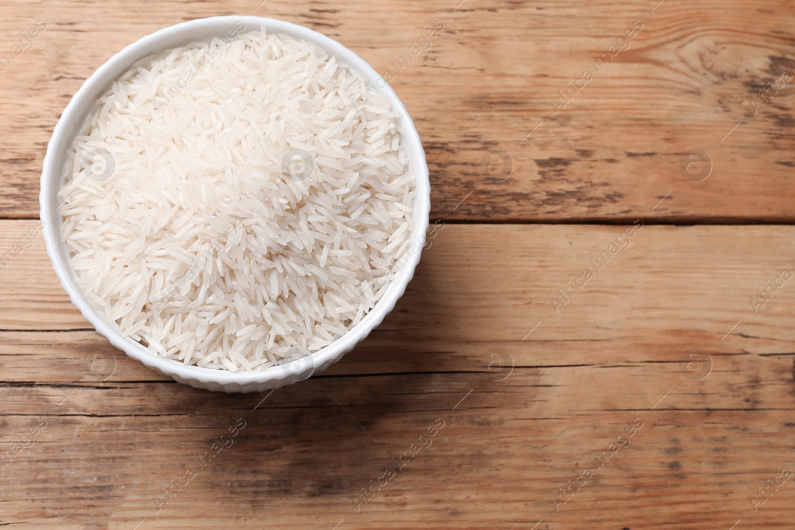 Photo of Raw basmati rice in bowl on wooden table, top view. Space for text