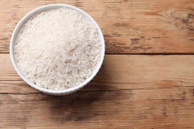 Photo of Raw basmati rice in bowl on wooden table, top view. Space for text