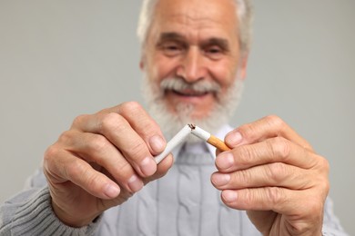 Photo of Stop smoking concept. Senior man breaking cigarette on light grey background, selective focus