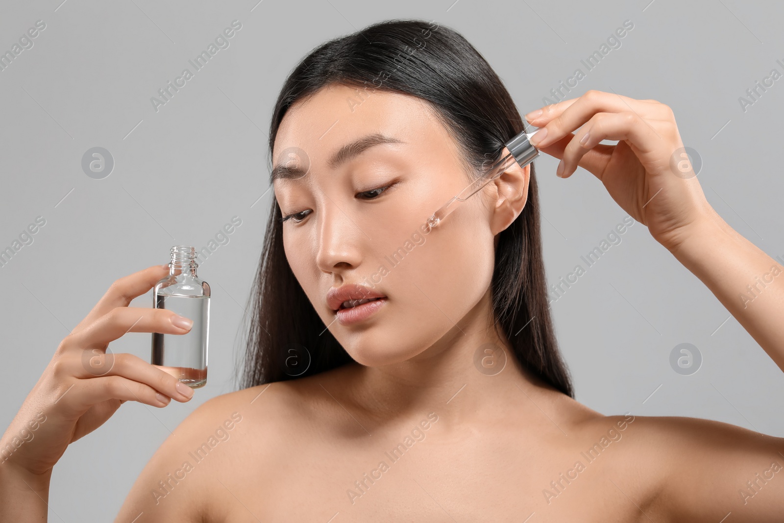 Photo of Beautiful young woman applying cosmetic serum onto her face on grey background