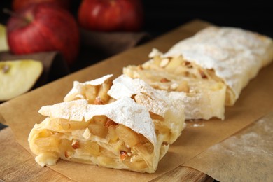 Photo of Delicious apple strudel with almonds and powdered sugar on wooden board, closeup