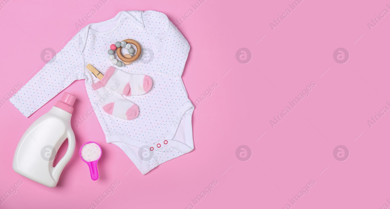 Photo of Flat lay composition with bottle of detergent and children's clothes on pink background. Space for text