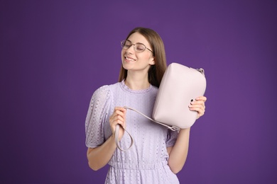 Young woman with stylish pink bag on purple background
