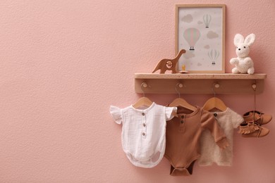 Photo of Wooden rack with cute baby clothes, shoes, toys and picture on pink wall indoors. Space for text