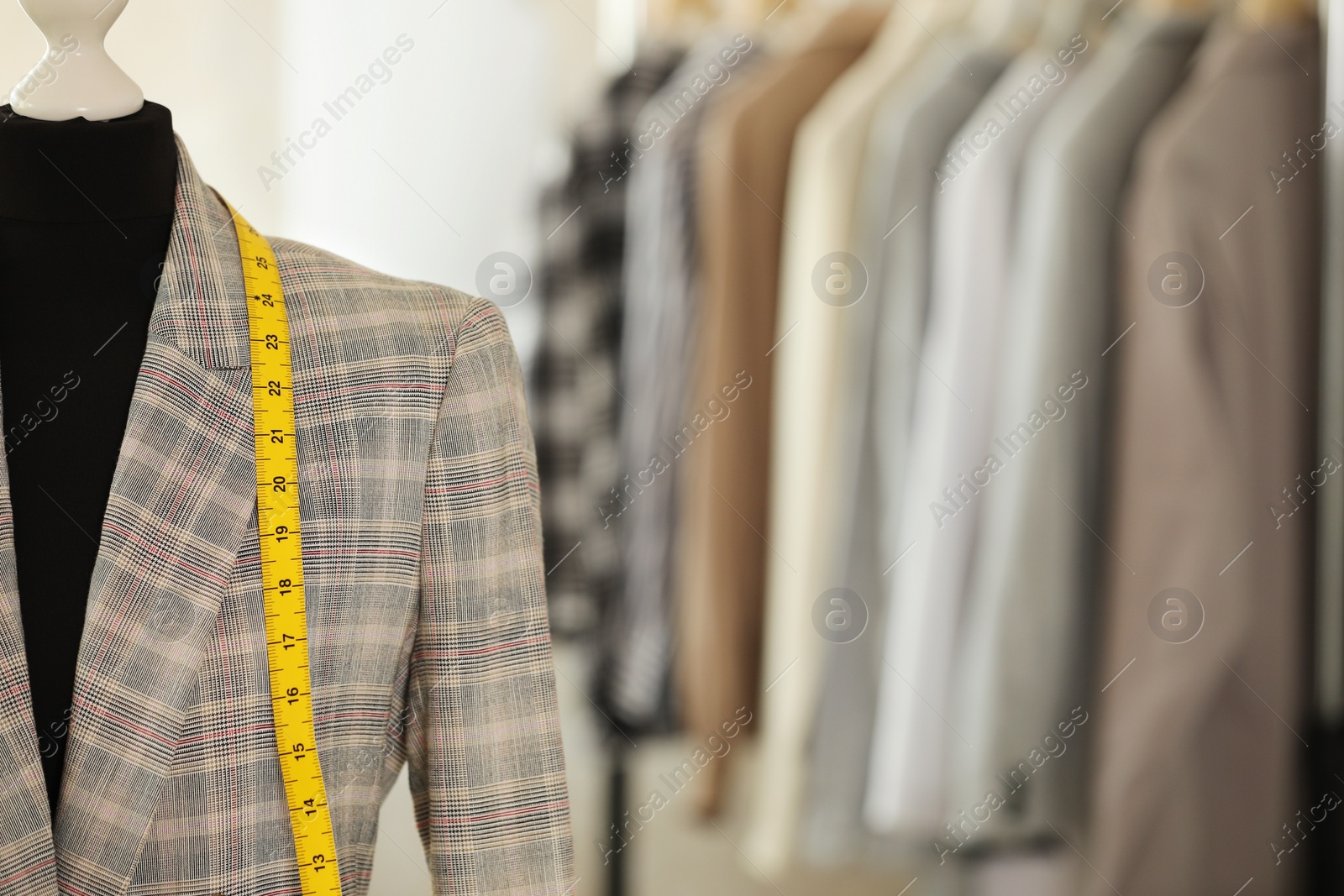 Photo of Mannequin with jacket and measuring tape in tailor shop, space for text