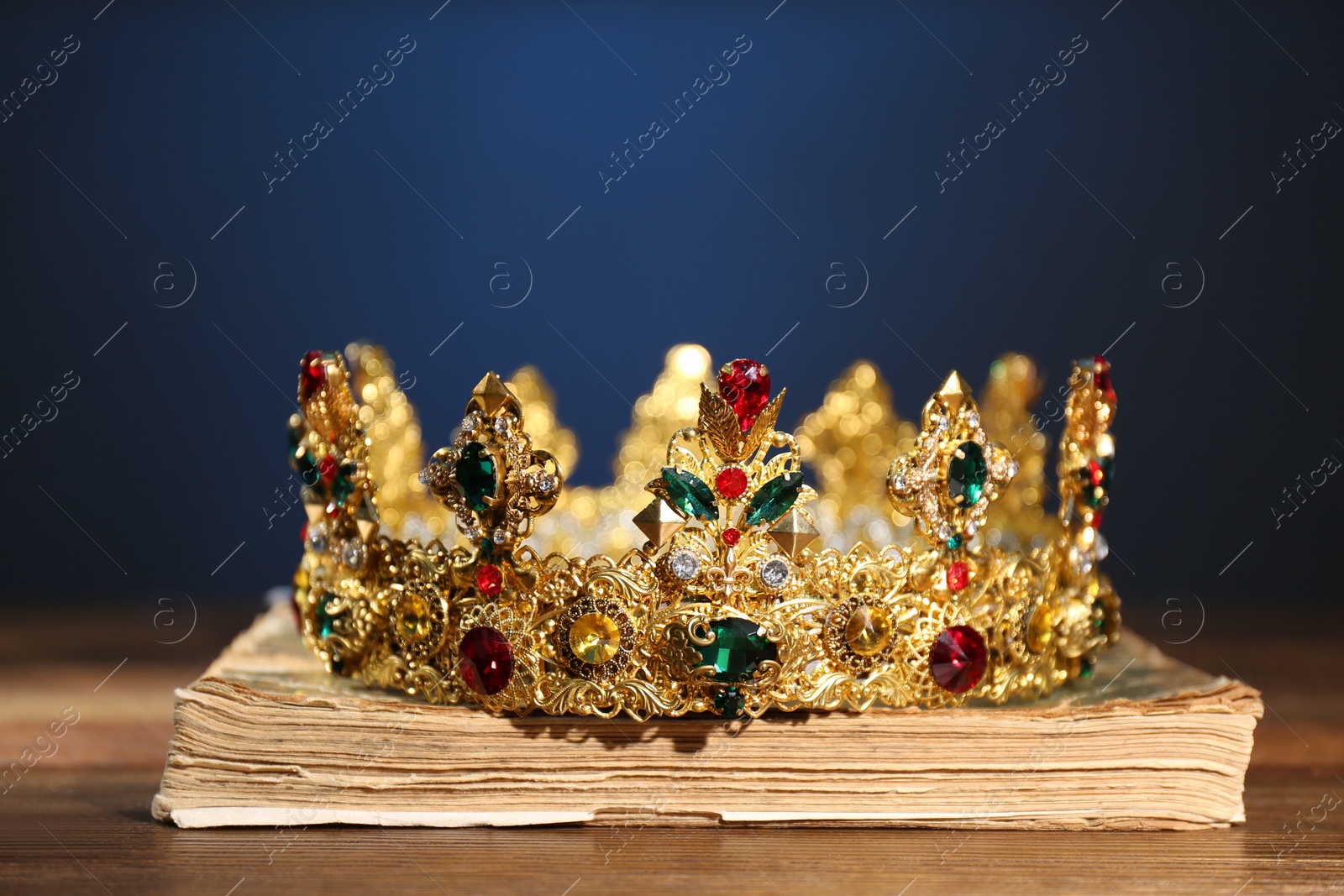Photo of Beautiful golden crown on old book against dark blue background. Fantasy item