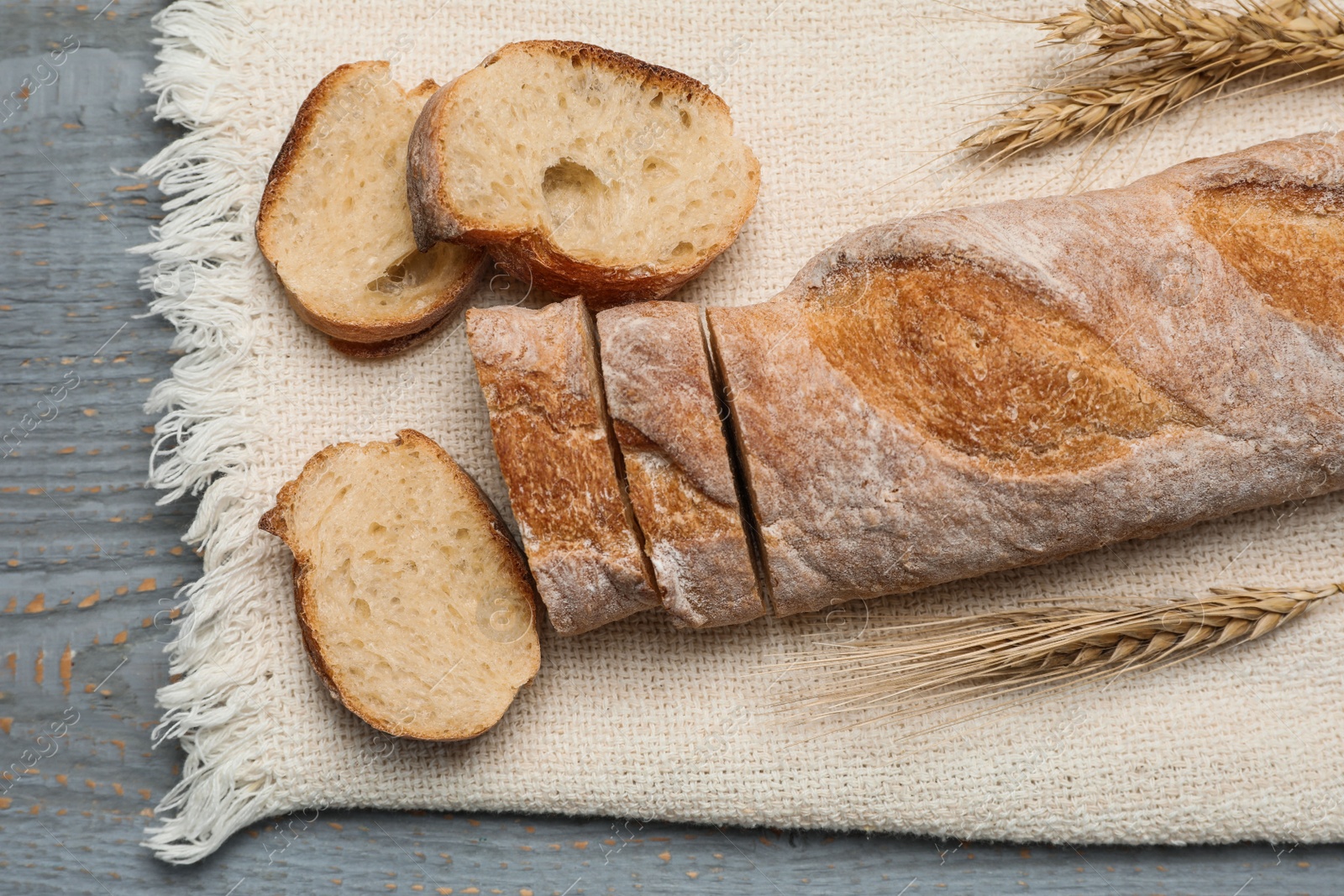 Photo of Cut delicious French baguette on grey wooden table, top view