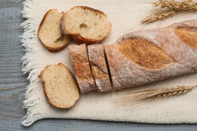 Cut delicious French baguette on grey wooden table, top view