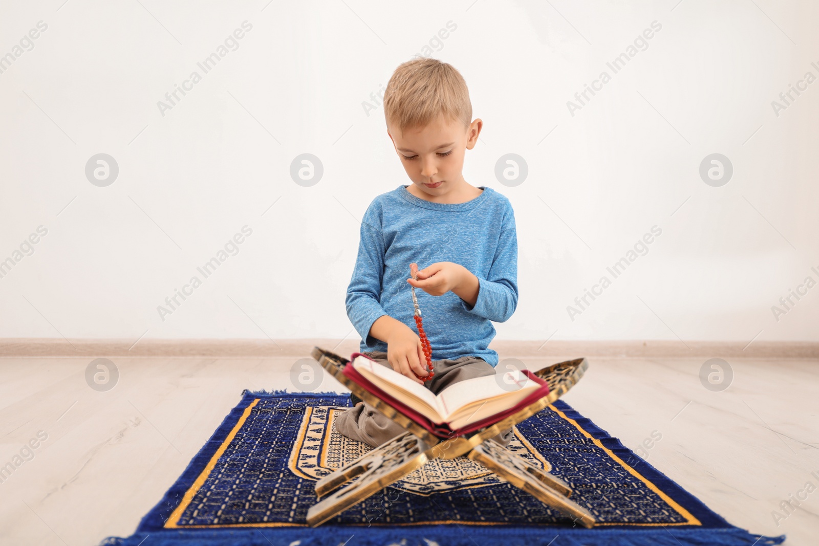 Photo of Little Muslim boy with misbaha and Koran praying on rug indoors