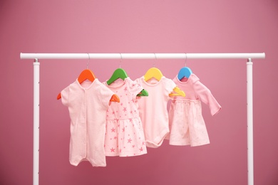 Baby clothes hanging on rack against color background